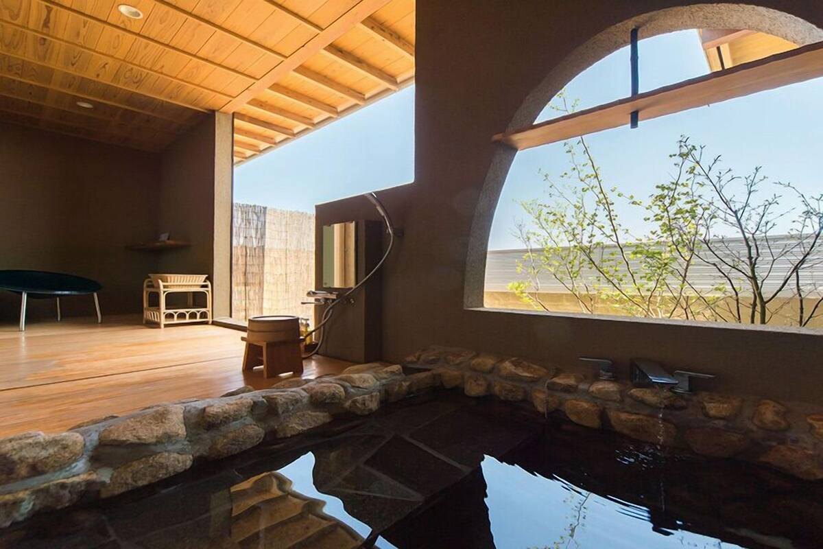 A modern interior with a stone-lined pool, wooden flooring, and a large window offering a view of the outdoors.