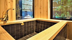 A traditional Japanese soaking tub with a wooden interior, a faucet, and a view of a garden through a window. - Kyorana Kyogetsutei (Kyoto)