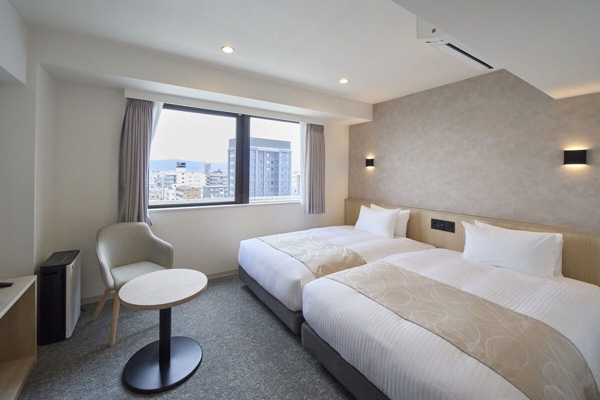 Habitación de hotel con dos camas, televisión, escritorio y ventana con vistas a la ciudad.