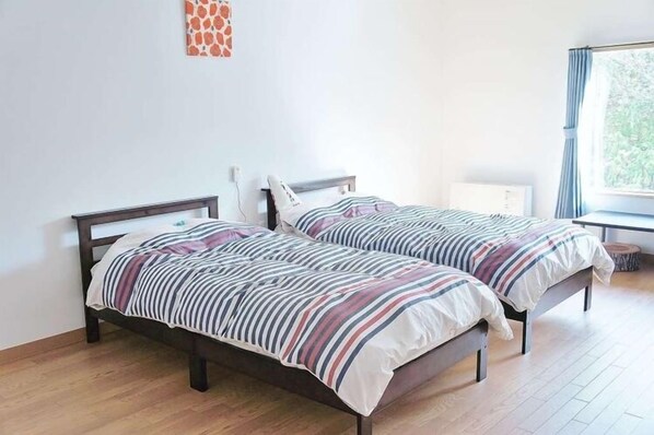 A bedroom with two beds, a window with curtains, and a wall-mounted radiator.