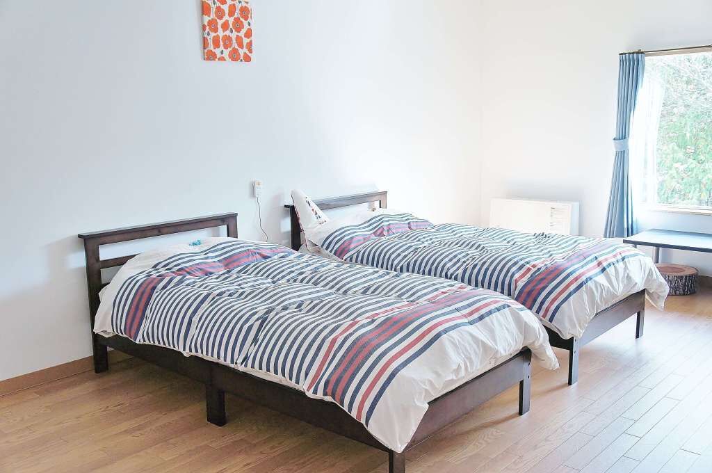 A bedroom with two beds, a window with curtains, and a radiator.