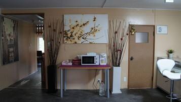 Una zona de recepción con mostrador, microondas, un florero con ramas y una silla blanca.