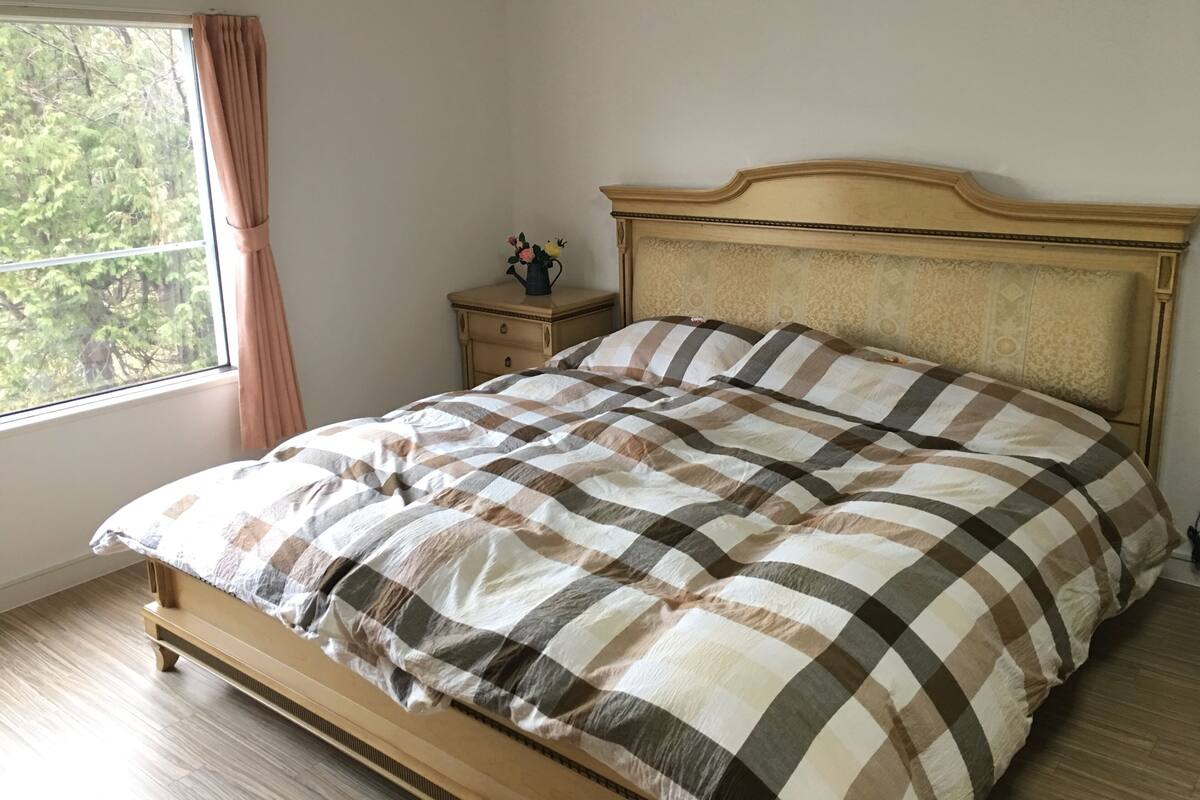 A bed with a checkered bedspread, a nightstand with a vase, and a window with curtains.