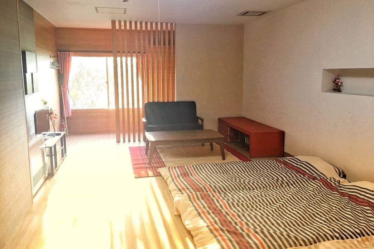 A hotel room with a bed, a sofa, a TV, a small table, and a window with curtains.