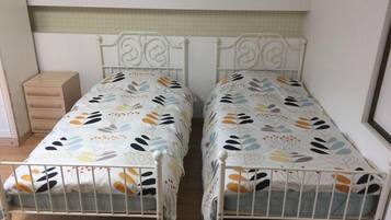 Quarto com duas camas de solteiro, um pequeno aparador de madeira e parede revestida de azulejos.