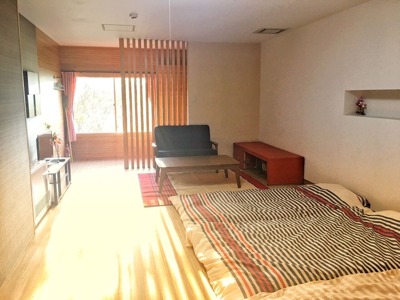A bedroom with a bed, a sofa, a TV, a small table, and a window with curtains.