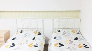 Una habitación con dos camas individuales de estructura metálica blanca, un aparador de madera y una pared de color claro.