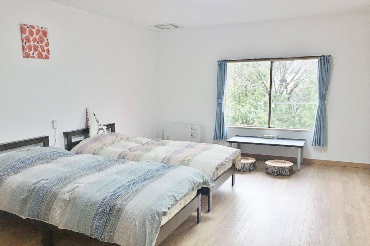 A bedroom with two beds, a window with curtains, a radiator, and a small table with a plant.