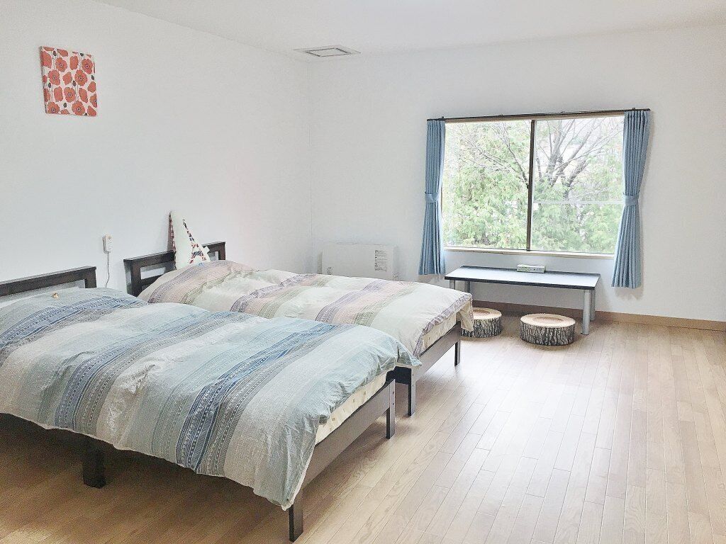 Un dormitorio con dos camas, una ventana con cortinas, un radiador y una mesita.