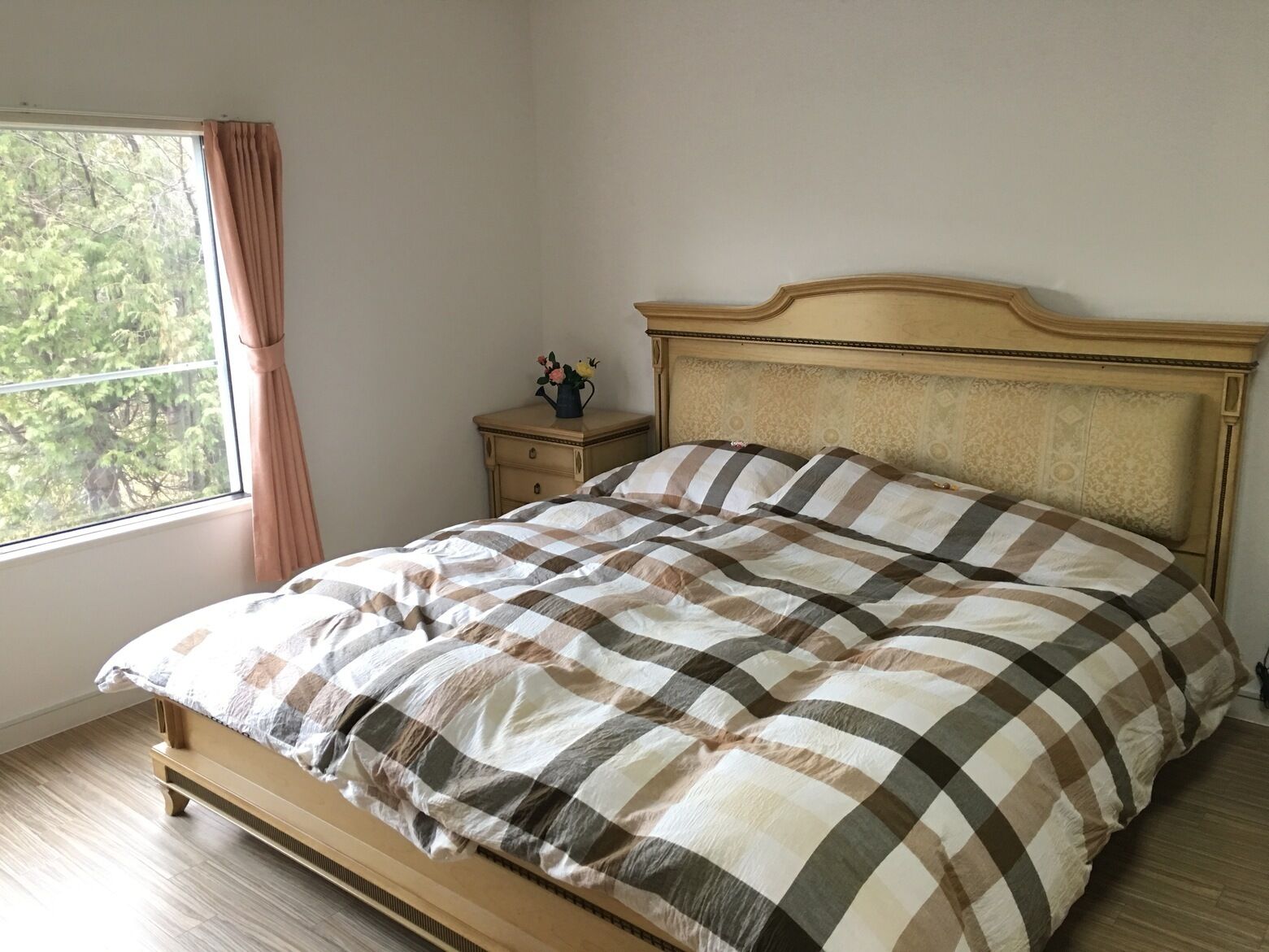 A bed with a checkered bedspread, a nightstand with a vase, and a window with curtains.