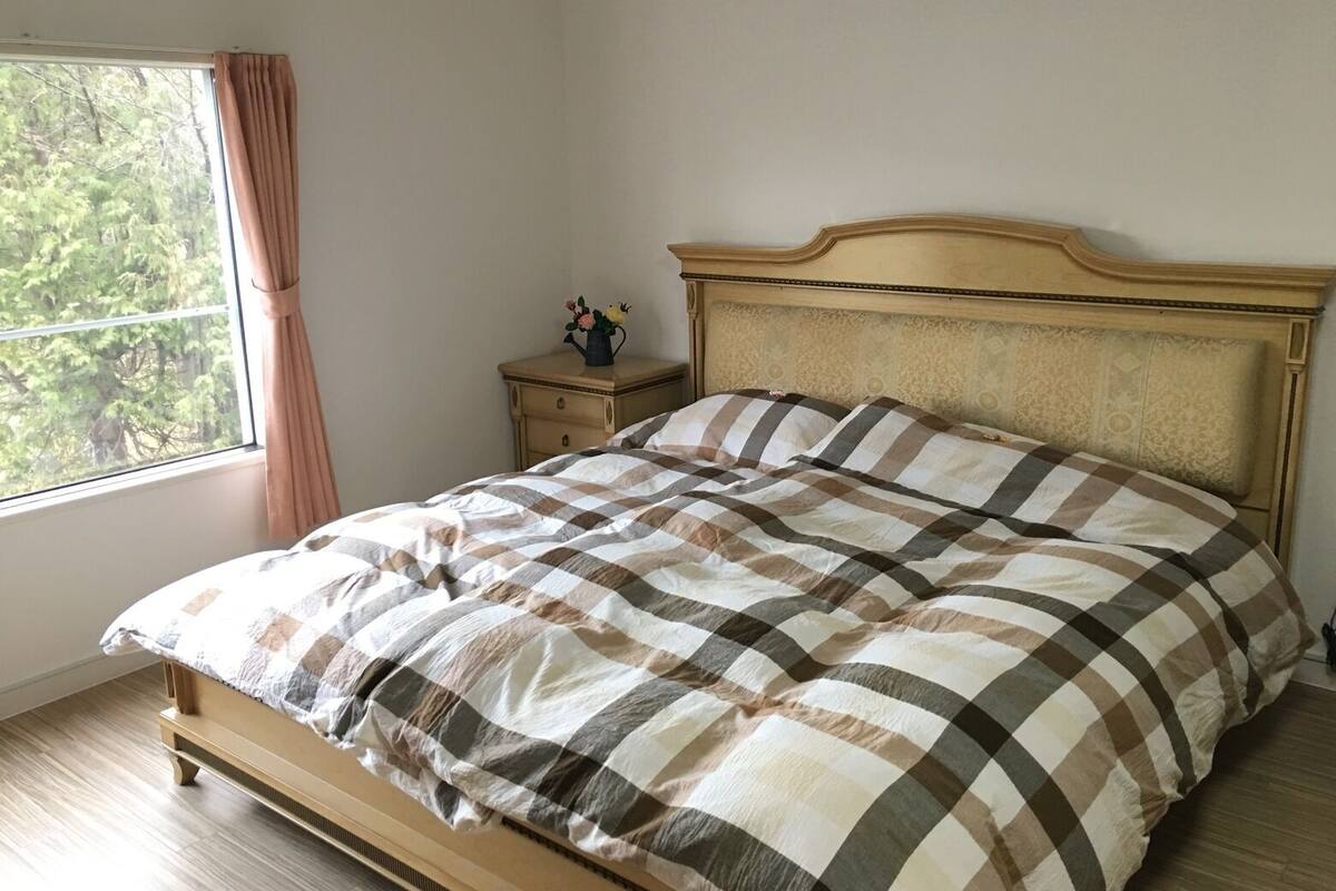 A bed with a checkered bedspread, a nightstand with a vase, and a window with curtains.