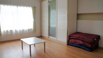 Quarto com piso de madeira, uma mesa branca, guarda-roupa com portas de vidro jateado e uma cama com cobertor vermelho.