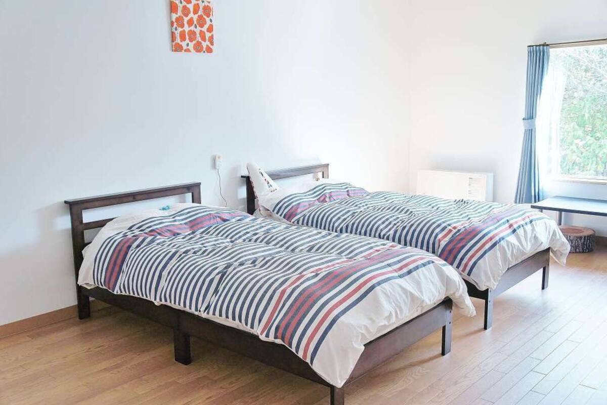 A bedroom with two beds, a window with curtains, and a radiator.