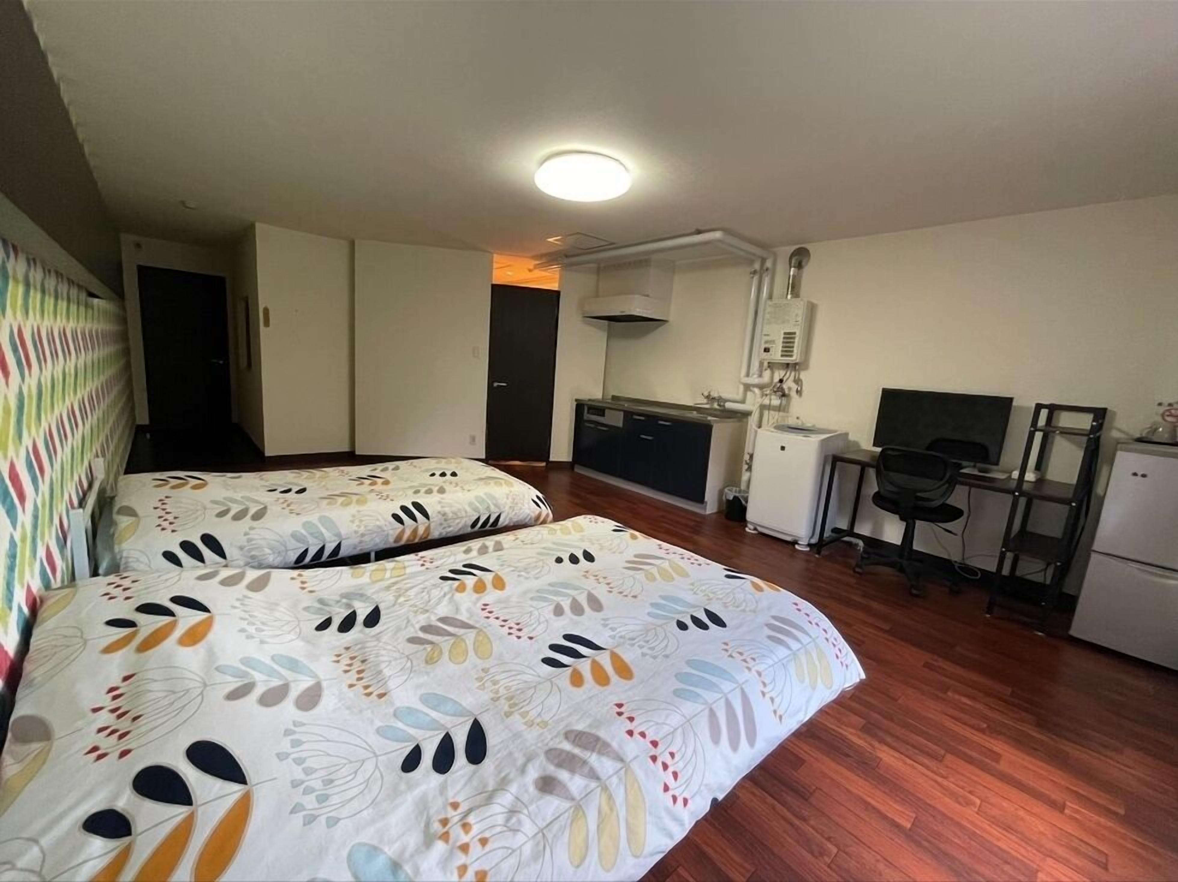 A room with two beds, a kitchenette, a desk with a computer, and a TV.