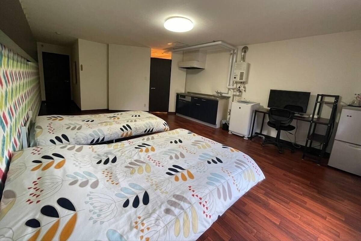 A room with two beds, a kitchenette, a desk with a computer, and a TV.