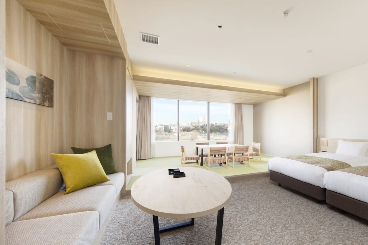 A hotel room with a sofa, a round table, a bed, and a dining area with chairs.