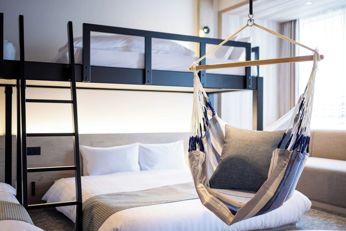 A bunk bed with a hammock chair, a bedside table, and a window with curtains.