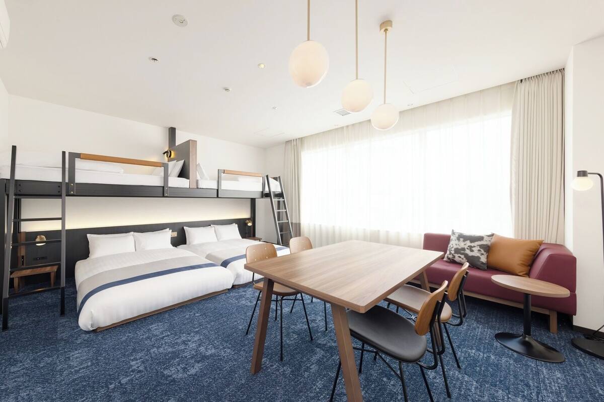 A hotel room with bunk beds, a dining table, a sofa, and a TV.