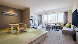 Ett modernt hotellrum med en matplats, soffa, TV och stora fönster med utsikt över staden.