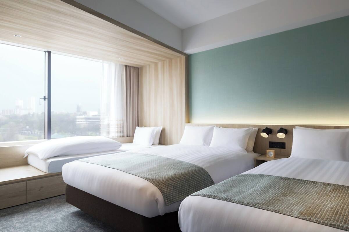 A hotel room with two beds, a large window with curtains, a view of the city, and a green accent wall.