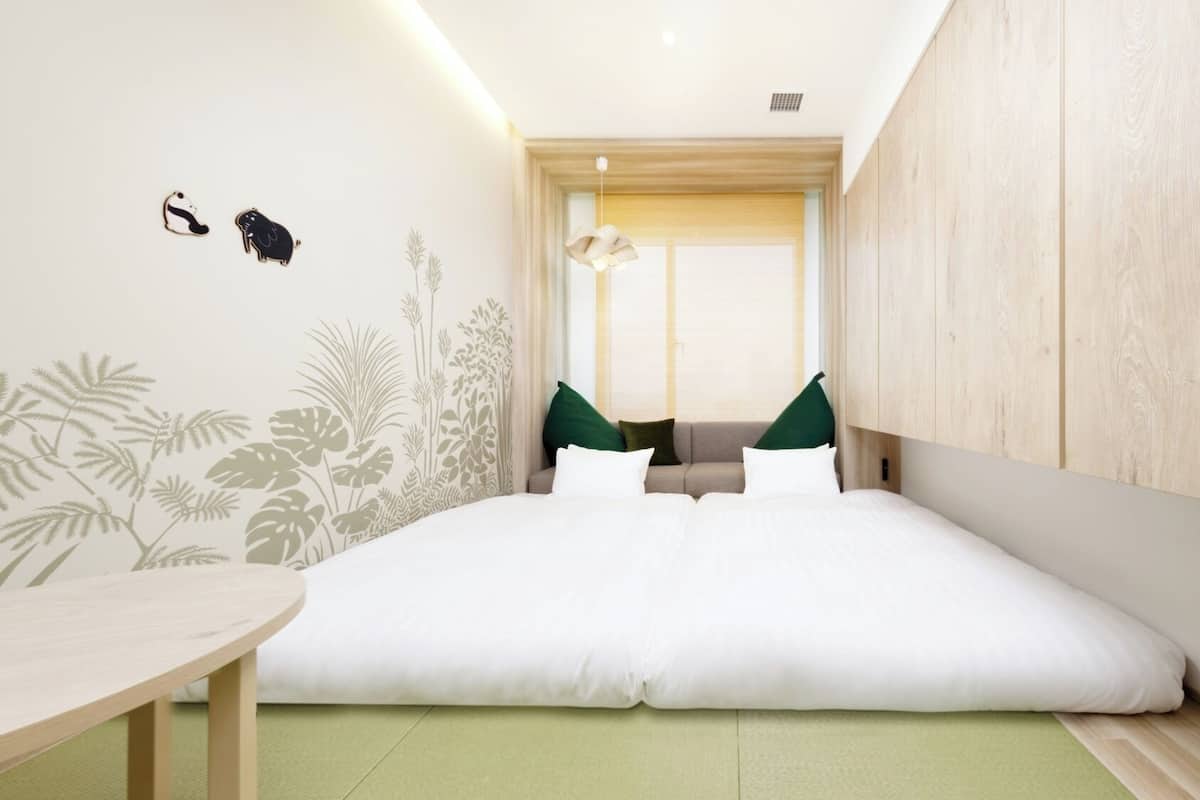 A modern hotel room with a bed, a small table, and a window with blinds.