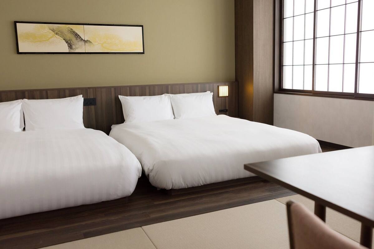 A hotel room with two beds, a wooden headboard, a large window, and a painting on the wall.