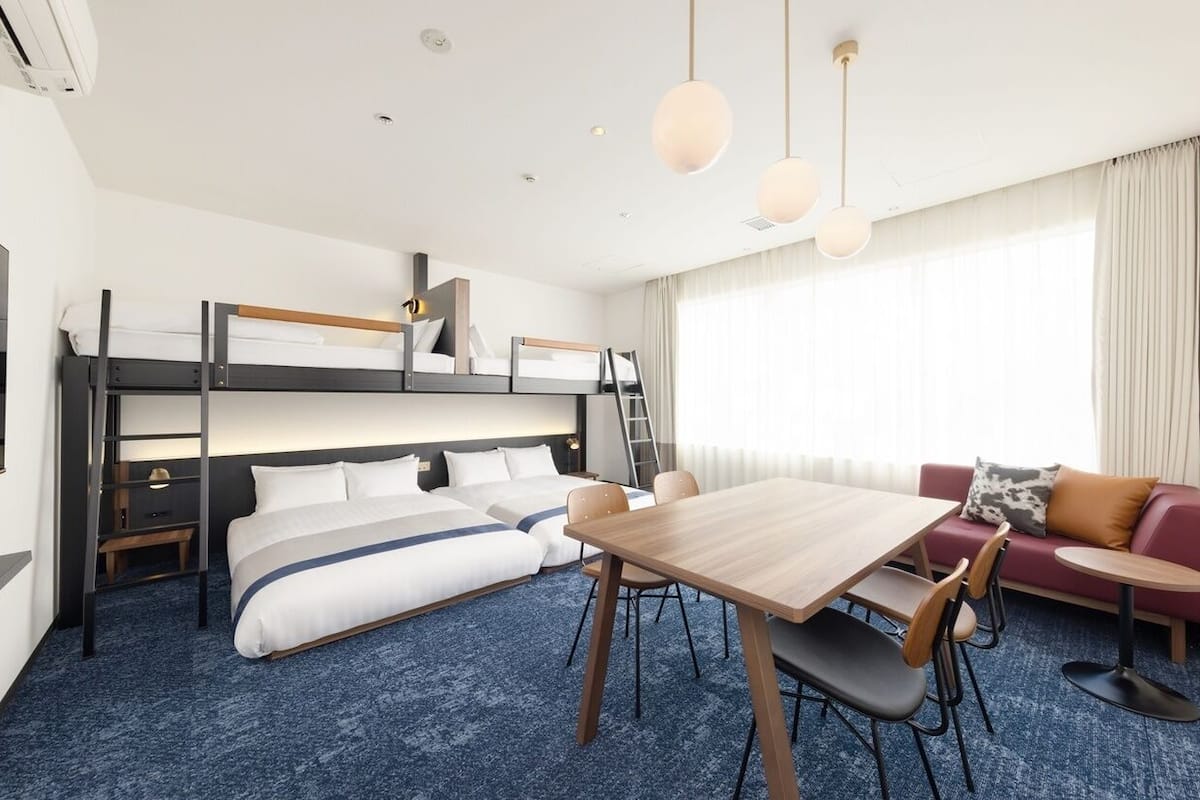 A hotel room with bunk beds, a dining table, a sofa, and a TV.