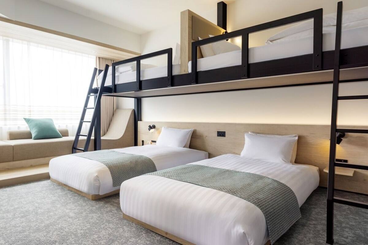 A hotel room with bunk beds, a sofa, and a window with curtains.