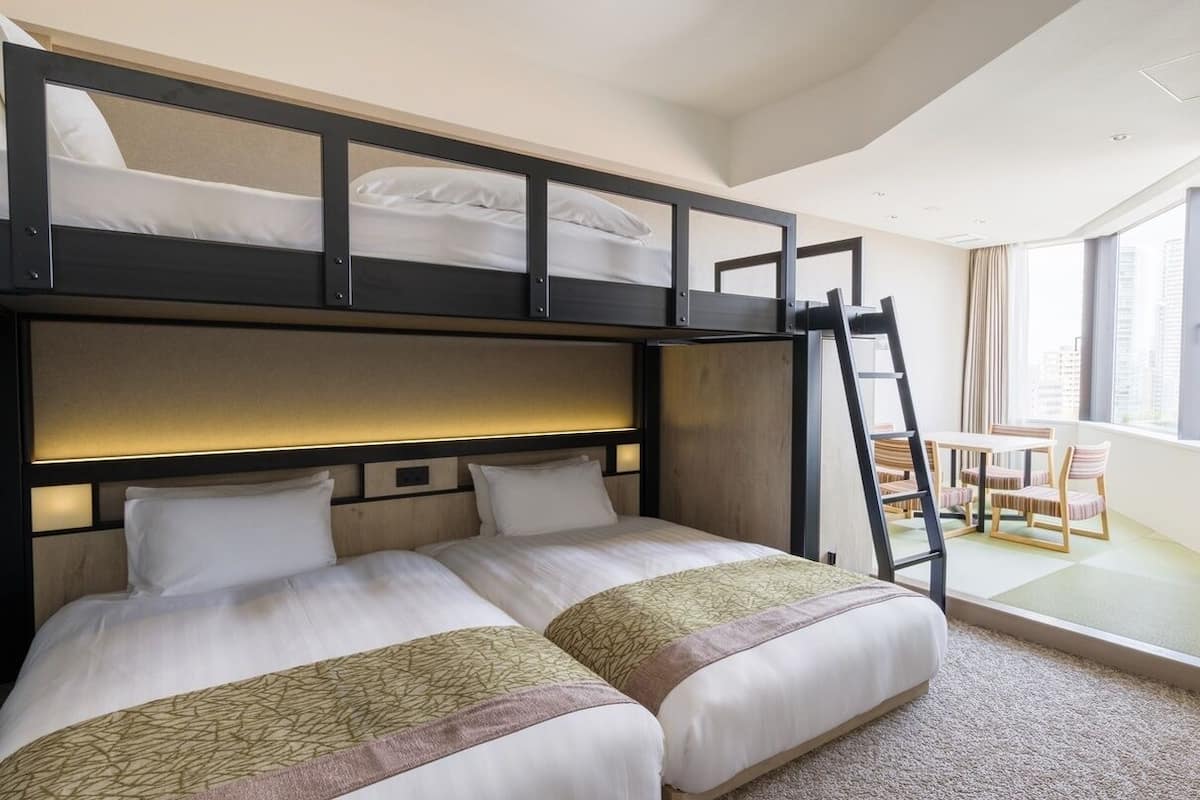 A hotel room with a bunk bed, a desk with a chair, and a window with curtains.