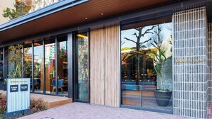 En modern byggnad med stora glasfönster, en träfasad och en skylt med texten "&Here Tokyo Ueno".