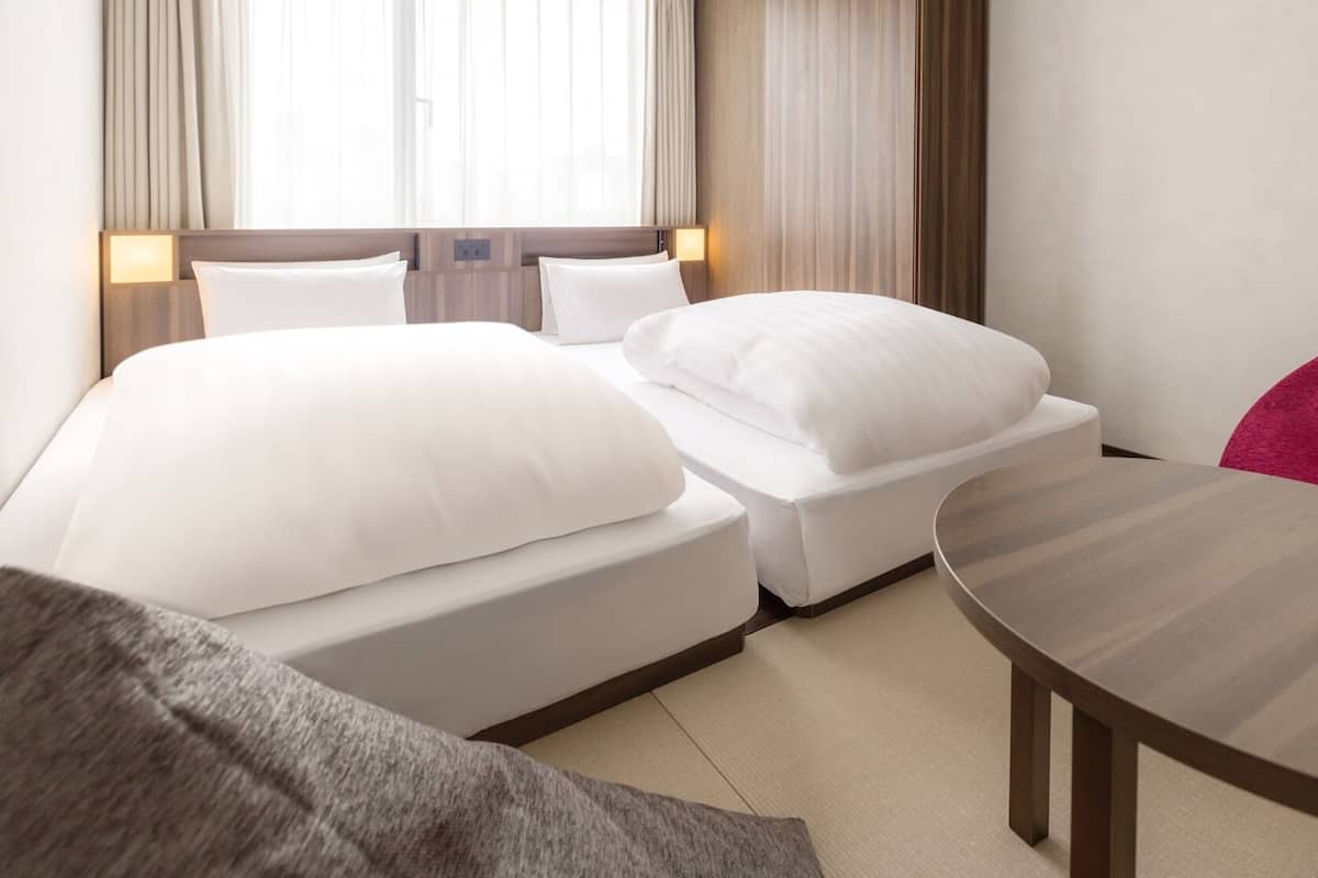 A hotel room with two beds, a round table, and a red pillow.