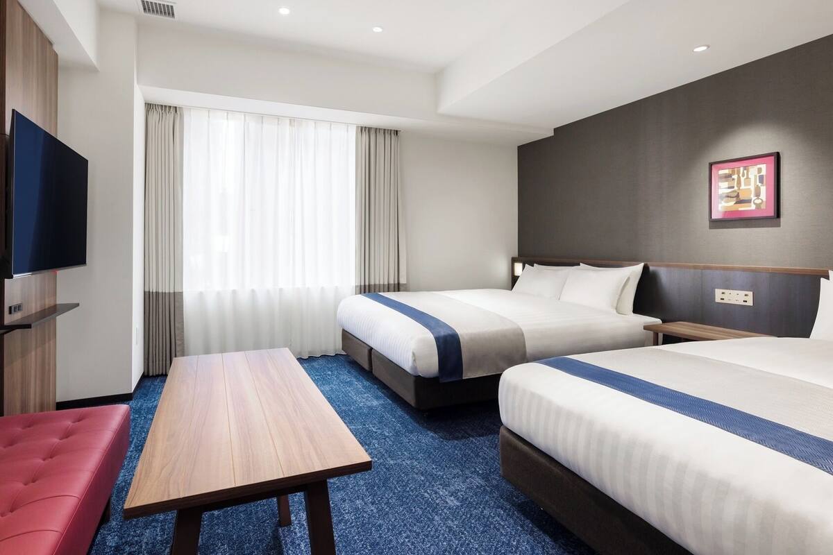 A hotel room with two beds, a flat-screen TV, a wooden table, and a red sofa.