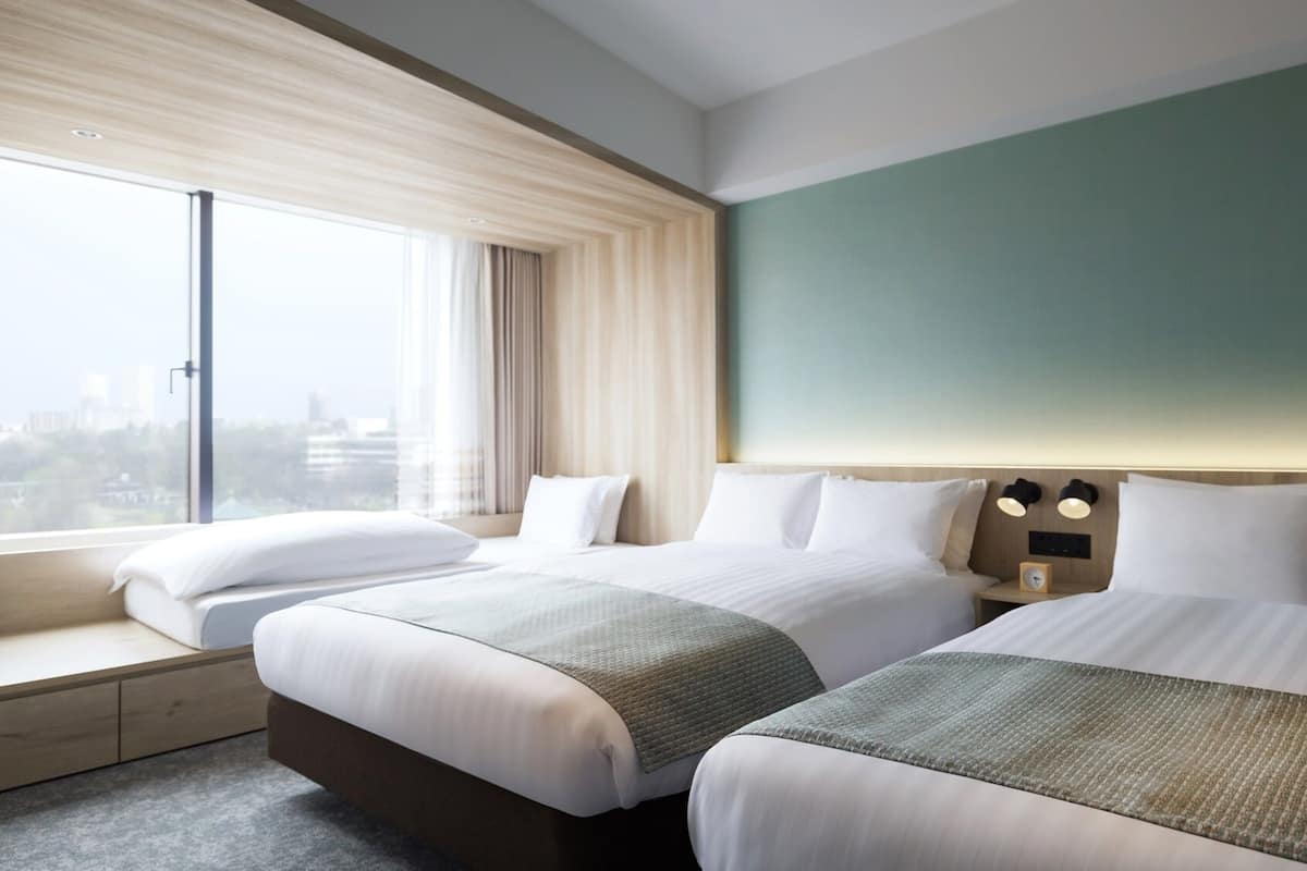 A hotel room with two beds, a large window, a view of the city, and a green accent wall.
