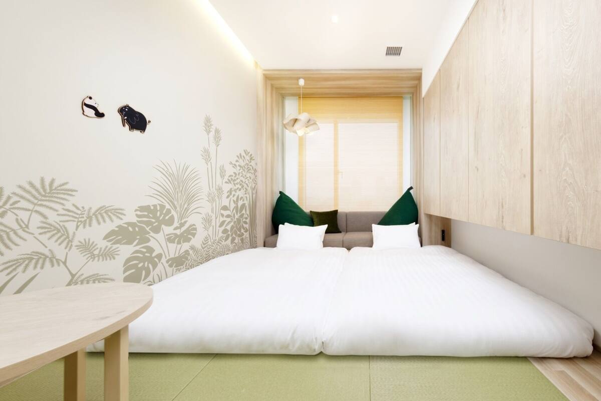 A bedroom with a bed, a small table, and a window with blinds.