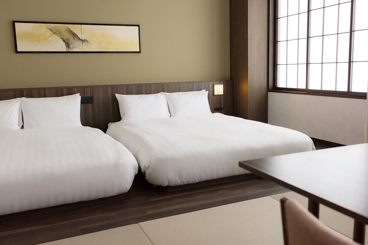 A hotel room with two beds, a wooden headboard, a large window, and a painting on the wall.