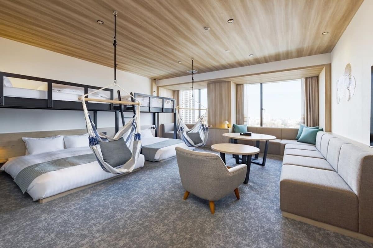A modern hotel room with a bunk bed, two hammocks, a sofa, a round table, and a TV.