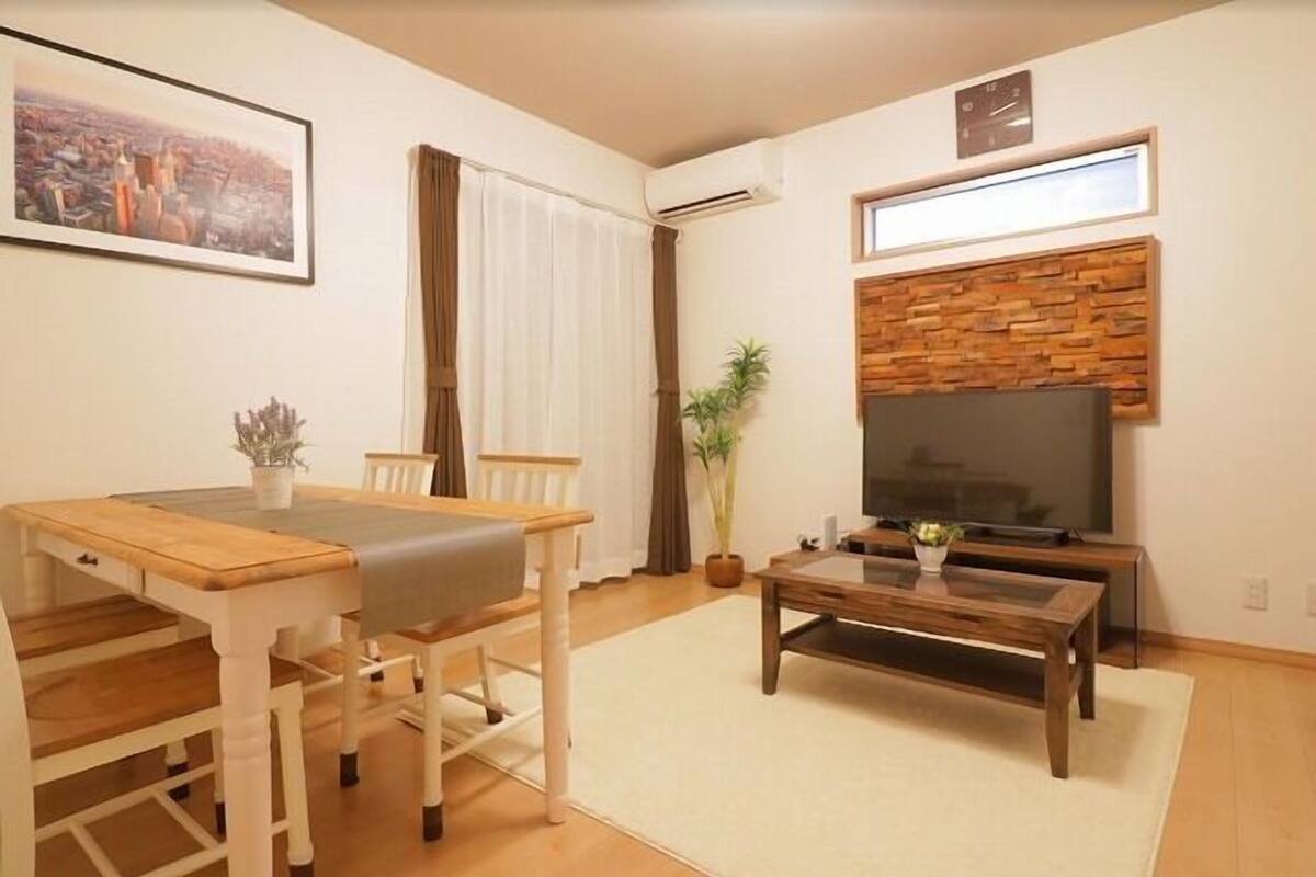 Ein Wohnzimmer mit Esstisch, Stühlen, Couchtisch, Fernseher und einer Pflanze.