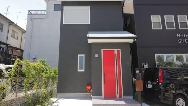Ein modernes Gebäude mit roter Tür, heller Fassade und einem abgestellten Fahrzeug.