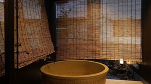 Un bain traditionnel de style japonais, doté d’un grand bassin en pierre, de stores en bambou et d’un petit jardin de rocaille.