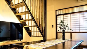 Un interior japonés tradicional con zona de comedor sobre tatami, televisor y puerta corredera.