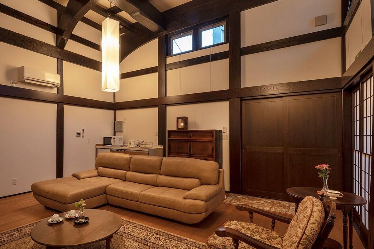 Una sala de estar con un sofá seccional, una mesa de centro, una mesita auxiliar, un armario y una ventana.