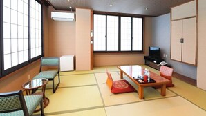 Una habitación de estilo japonés tradicional, con suelo de tatami, una mesa baja con cojines, televisión y puertas correderas.