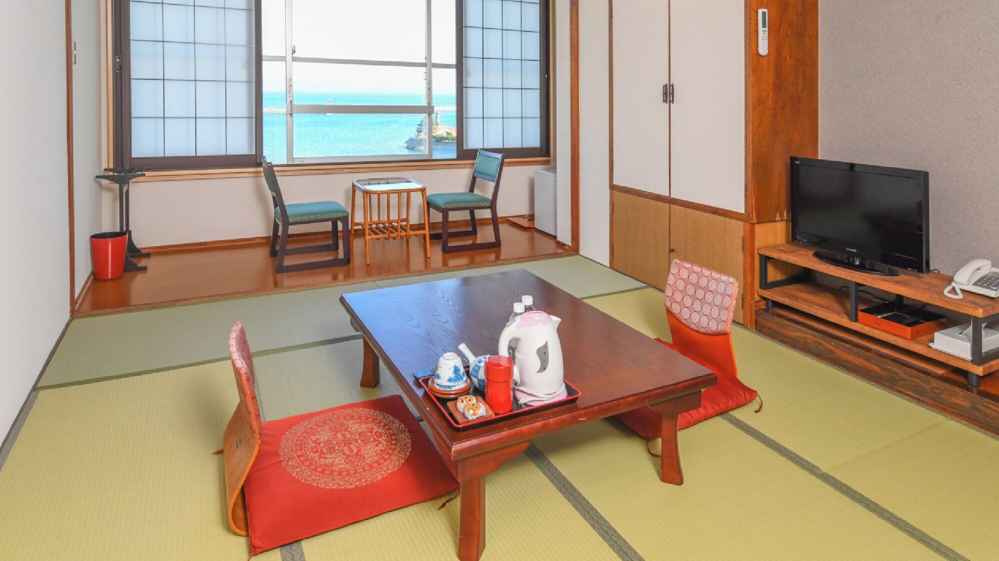 Une pièce de style japonais traditionnel, avec un sol recouvert de tatamis, une petite table basse avec un service à thé, un téléviseur et une vue sur la mer.