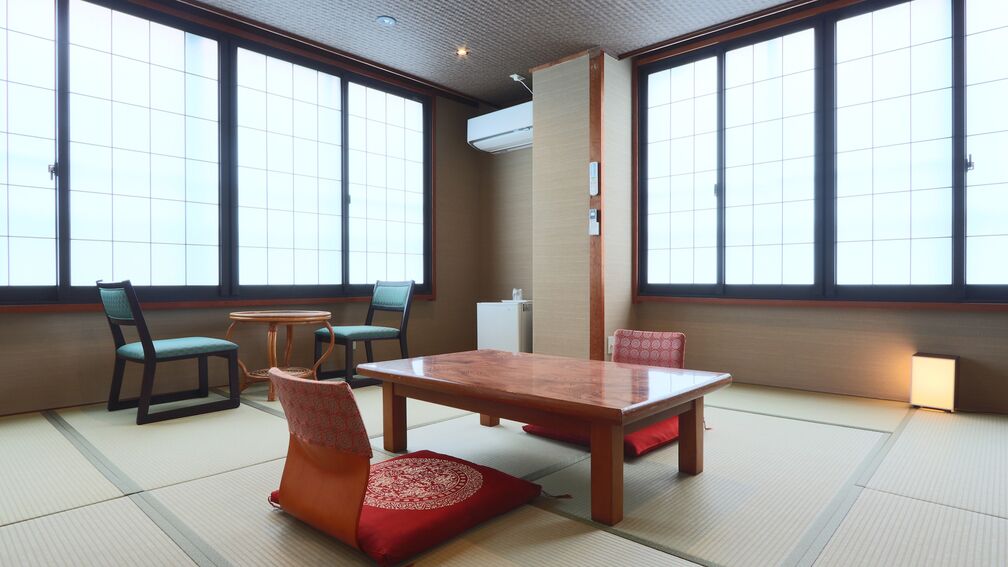 A tatami mat room with a wooden table, chairs, and a traditional Japanese air conditioning unit.