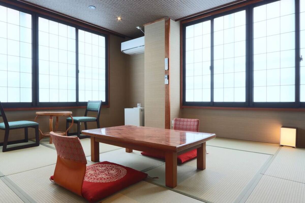 A tatami mat room with a wooden table, chairs, and a traditional Japanese air conditioning unit.
