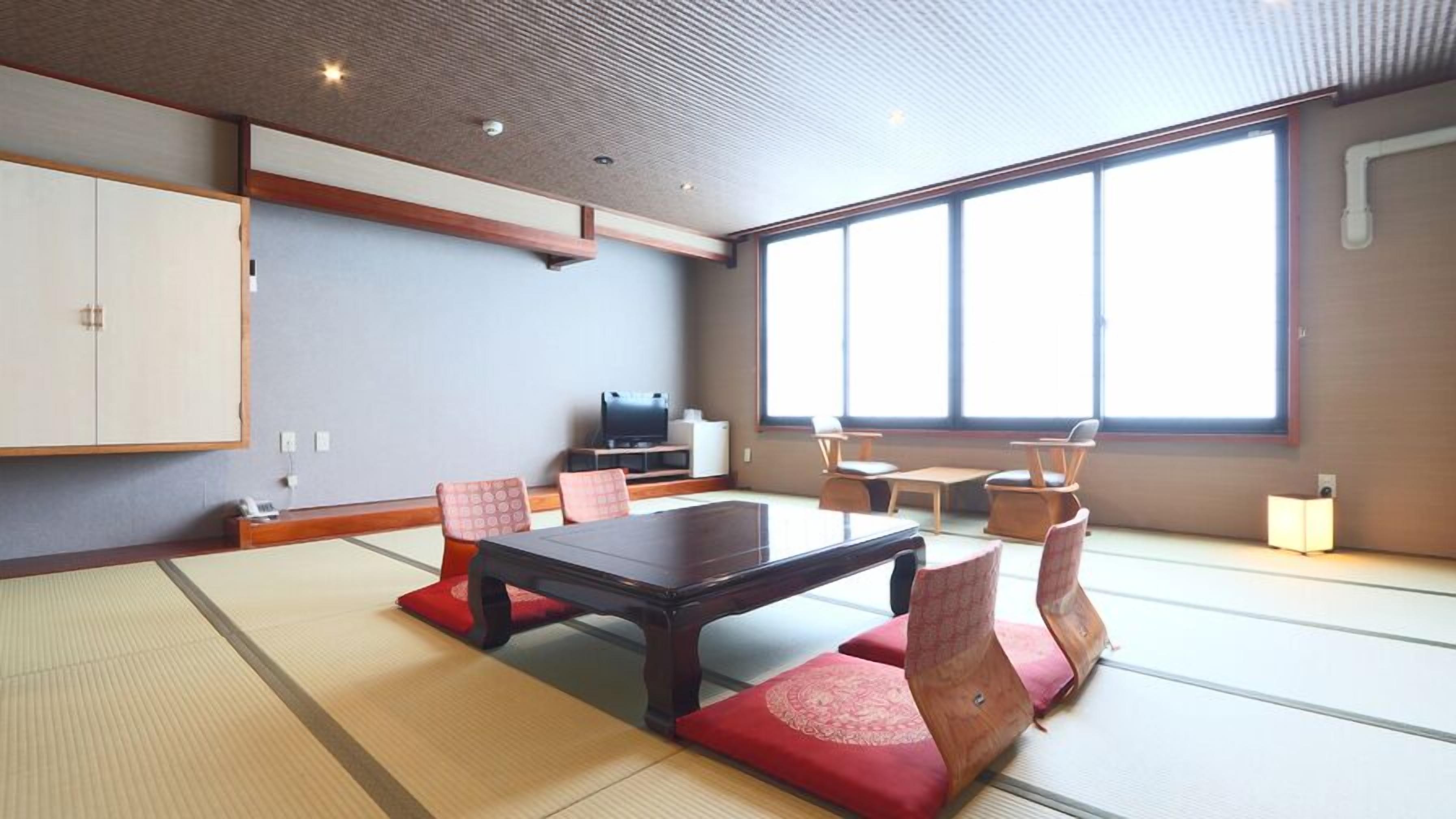 A tatami mat room with a low table, chairs, a cabinet, and a TV.