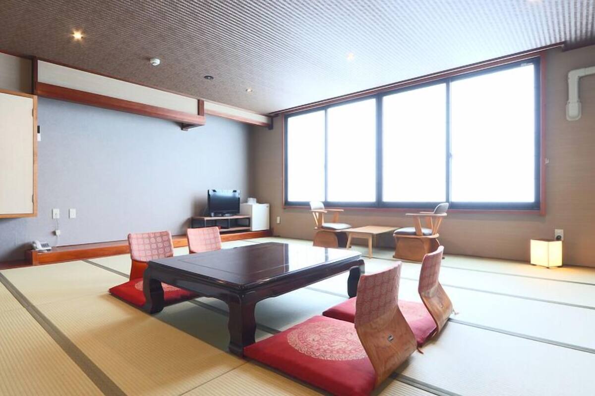 A tatami mat room with a low table, chairs, a cabinet, and a TV.