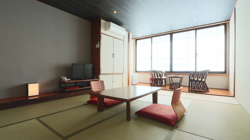 A traditional Japanese room with tatami flooring, a low table, two chairs, a television, and a sliding door.