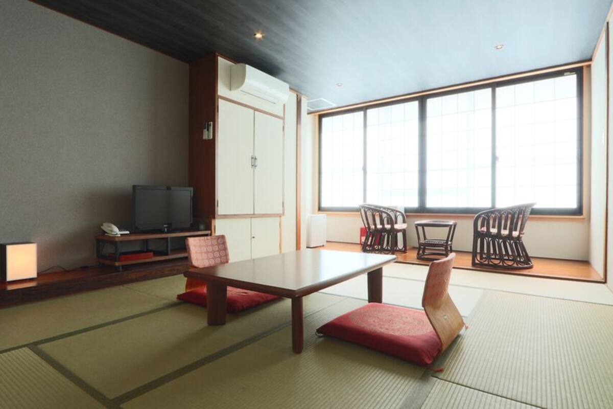 A traditional Japanese room with tatami flooring, a low table, two chairs, a television, and a sliding door.