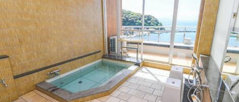 Un baño con jacuzzi de vidrio, suelo de baldosas y vistas a un balcón con piscina.